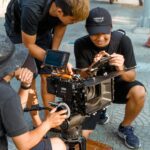 Filmmakers adjusting camera equipment on set outdoors, showcasing collaborative effort.